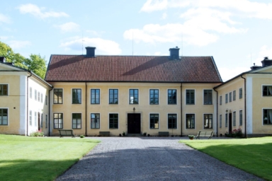 En gul byggnad vid en gräsmatta med en grusgång.