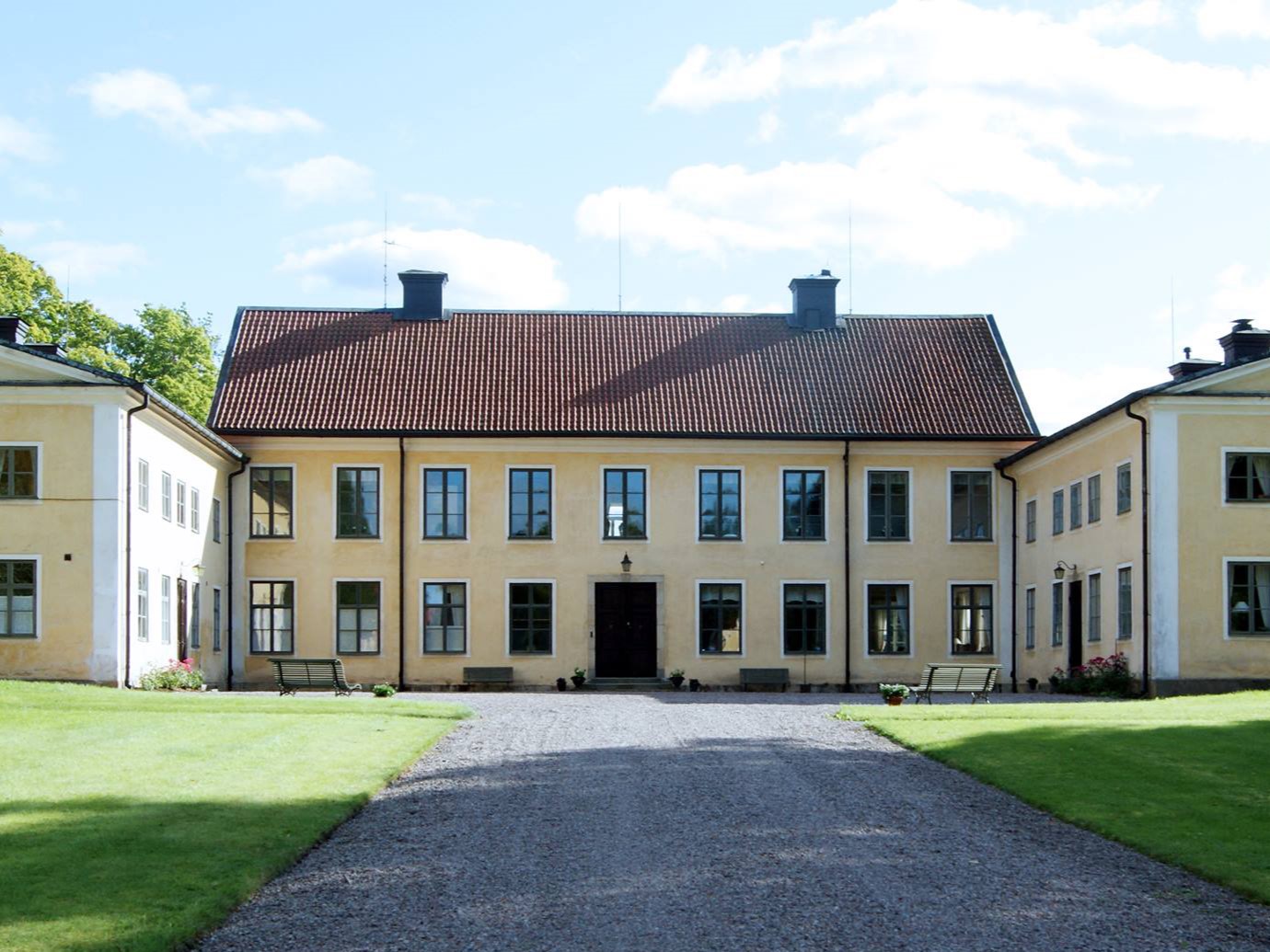 En gul byggnad vid en gräsmatta med en grusgång.