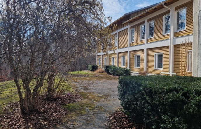 Ett gult hus vid buskar och träd.