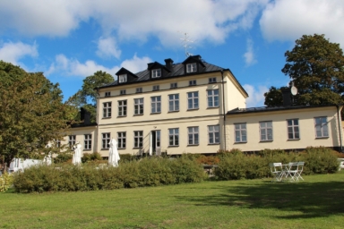 En ljus byggnad med trädgård och buskar framför.