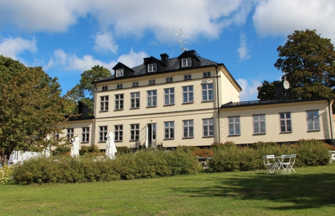 En ljus byggnad med trädgård och buskar framför.