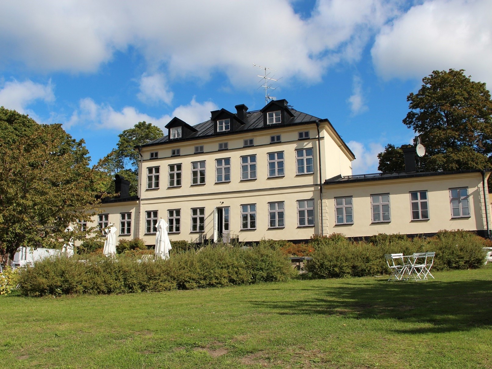 En ljus byggnad med trädgård och buskar framför.