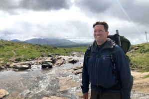 En man med ryggsäck står vid en fjällbäck.