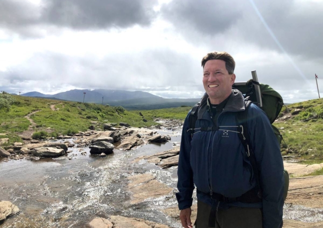 En man med ryggsäck står vid en fjällbäck.