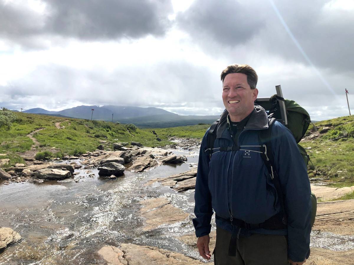 En man med ryggsäck står vid en fjällbäck.