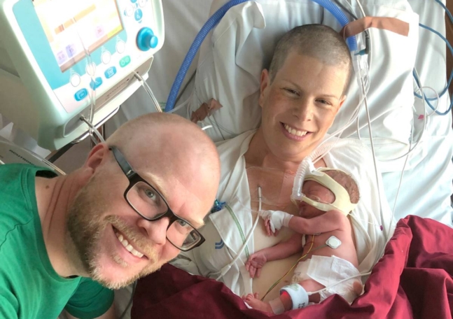 En kvinna med sin nyfödda bebis på sjukhuset och hennes man bredvid.