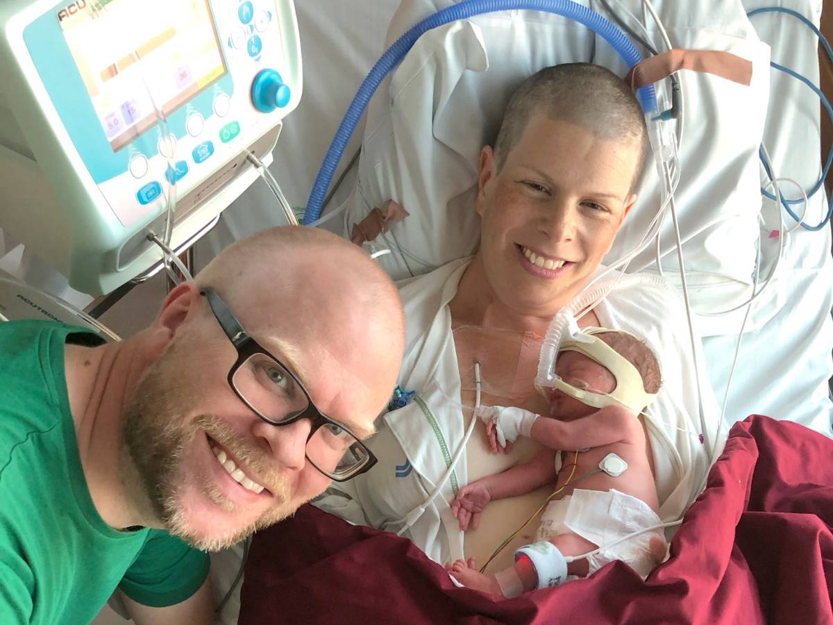 En kvinna med sin nyfödda bebis på sjukhuset och hennes man bredvid.