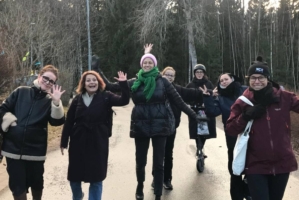 En grupp unga kvinnor går utomhus, ler och vinkar glatt mot kameran.