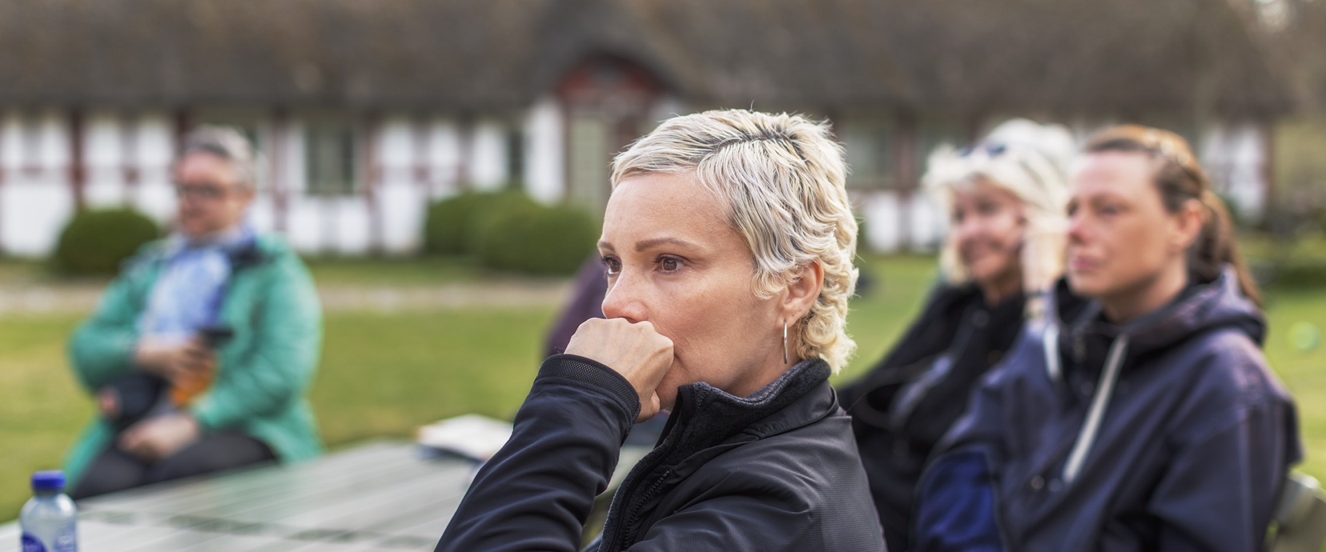 En grupp kvinnor sitter vid ett bord utomhus och lyssnar till en föreläsning.