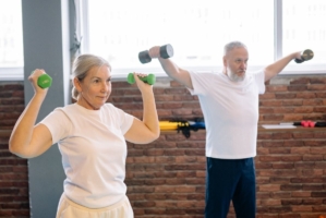 En äldre kvinna och man tränar med hantlar i en träningslokal.