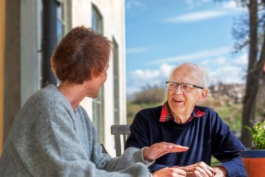 Ingemar Sjöberg sitter vid ett bord utomhus och samtalar med en deltagare på CancerRehabFondens rehabprogram.