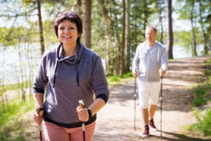 En medelålders kvinna och man är ute i skogen och går med stavar.