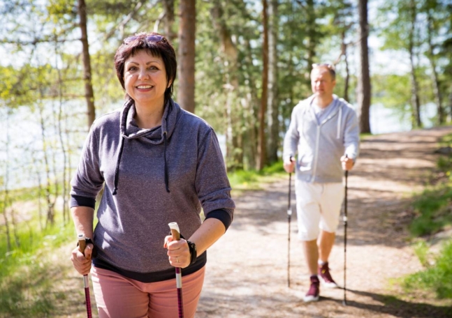 En medelålders kvinna och man är ute i skogen och går med stavar.