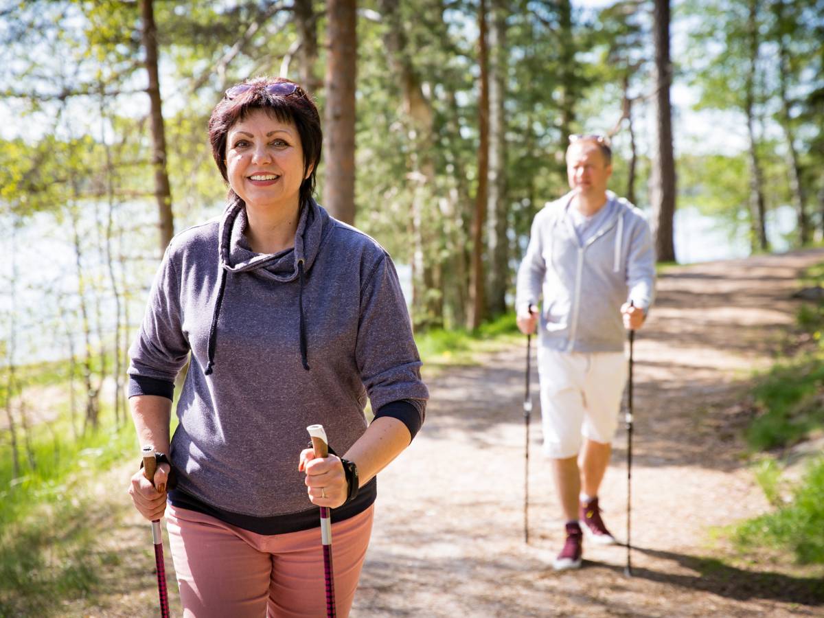 En medelålders kvinna och man är ute i skogen och går med stavar.