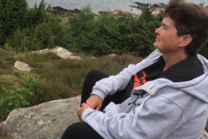 En kvinna sitter på en klippa och blickar ut över vattnet.