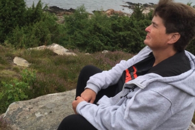 En kvinna sitter på en klippa och blickar ut över vattnet.