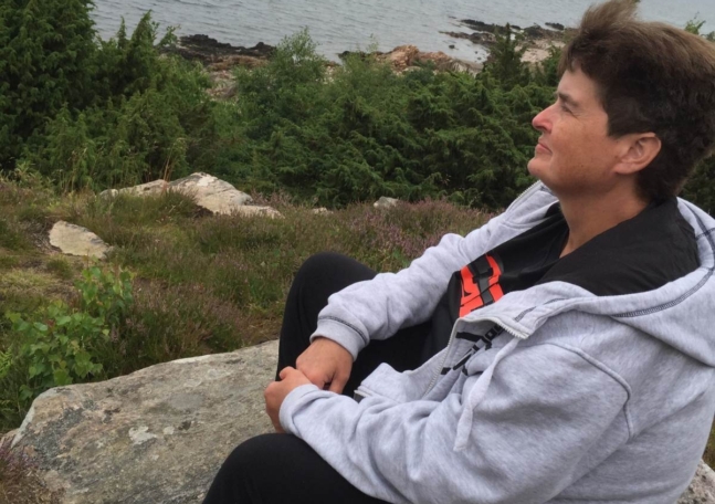 En kvinna sitter på en klippa och blickar ut över vattnet.