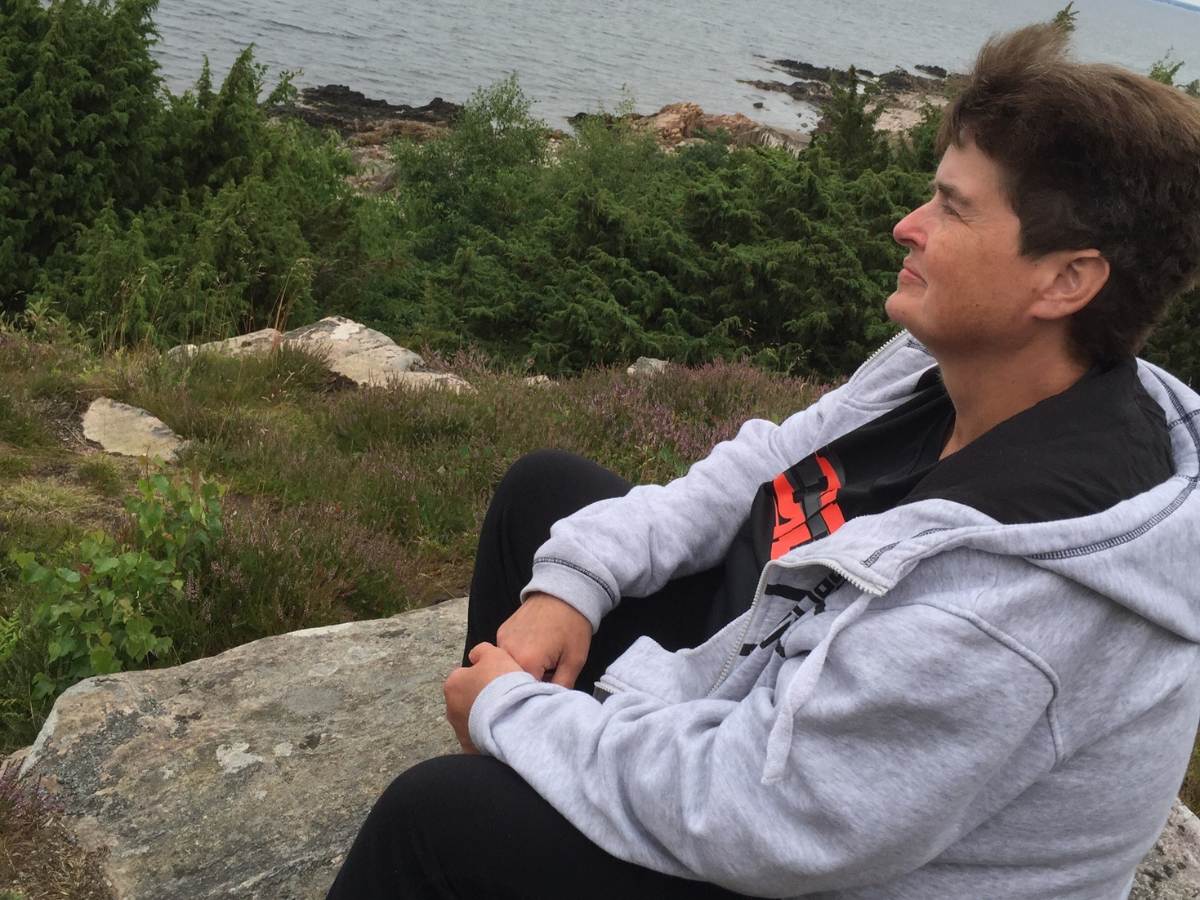 En kvinna sitter på en klippa och blickar ut över vattnet.