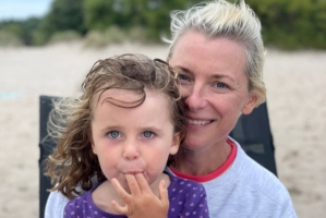 En kvinna sitter på stranden i en solstol med sin lilla dotter i famnen.