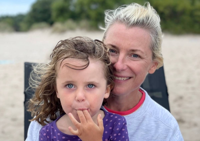 En kvinna sitter på stranden i en solstol med sin lilla dotter i famnen.