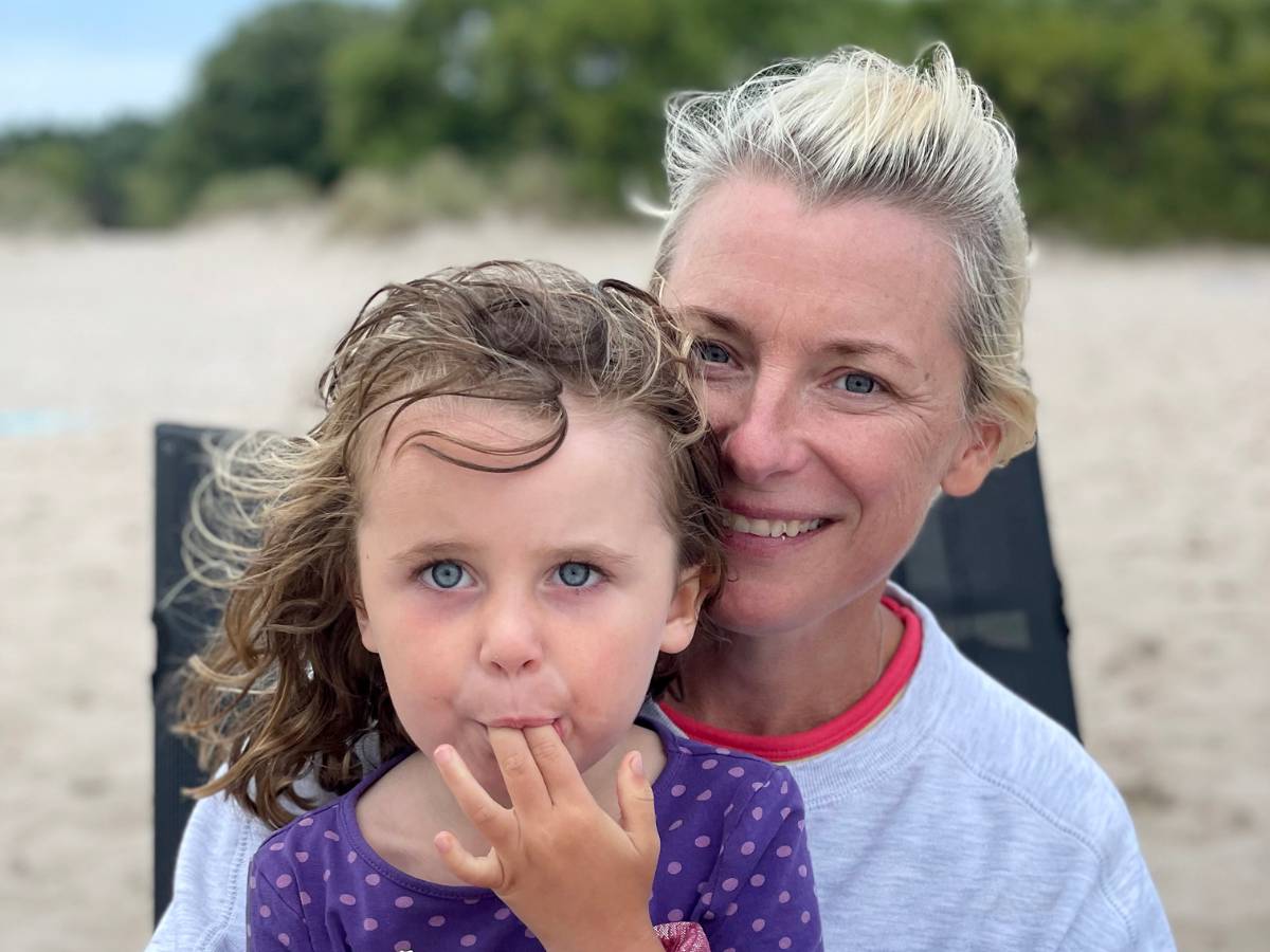 En kvinna sitter på stranden i en solstol med sin lilla dotter i famnen.