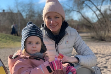 En mamma i vit jacka och hennes dotter i rosa jacka på en lekplats.