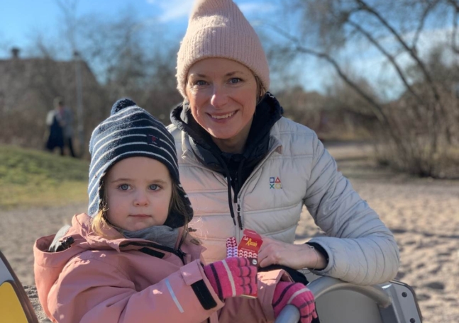 En mamma i vit jacka och hennes dotter i rosa jacka på en lekplats.