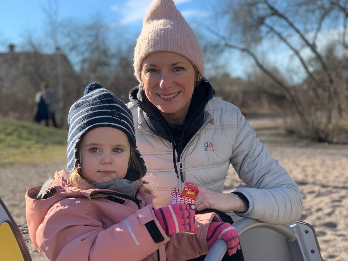 En mamma i vit jacka och hennes dotter i rosa jacka på en lekplats.