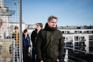 En man står på sin balkong med sina tre söner i bakgrunden.