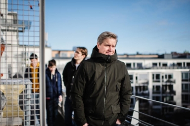 En man står på sin balkong med sina tre söner i bakgrunden.