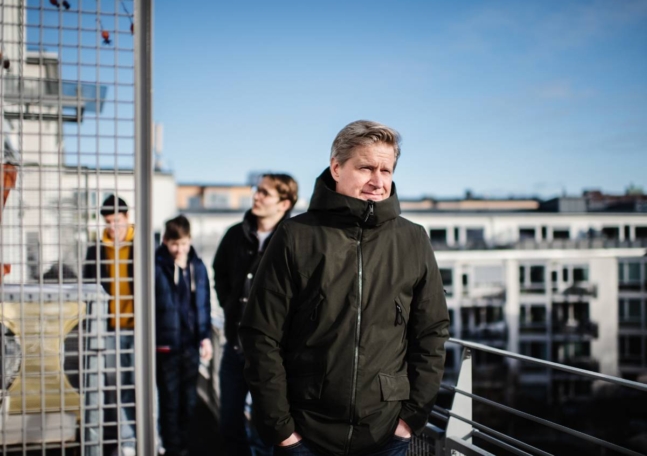 En man står på sin balkong med sina tre söner i bakgrunden.