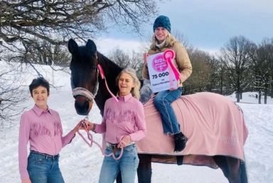 Pia Watkinson från CancerRehabFonden sitter på en häst och håller upp en check från Ride against cancer.