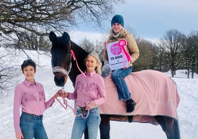 Pia Watkinson från CancerRehabFonden sitter på en häst och håller upp en check från Ride against cancer.