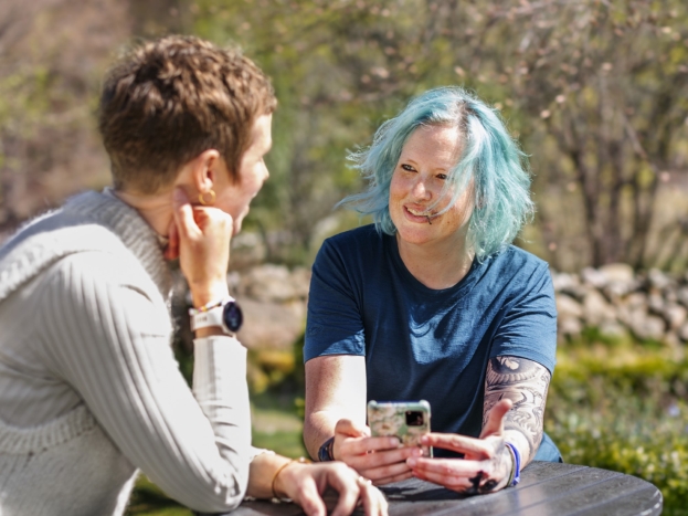 Två kvinnor sitter utomhus vid ett bort och samtalar.