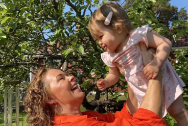 En kvinna ler och håller upp sitt barnbarn.