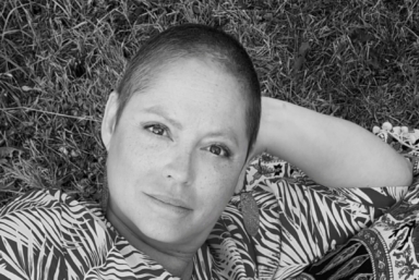 En kvinna med kort hår ligger i gräset och tittar in i kameran.