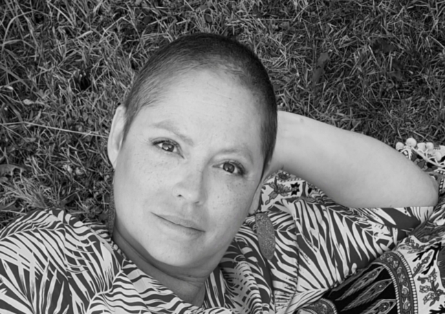 En kvinna med kort hår ligger i gräset och tittar in i kameran.