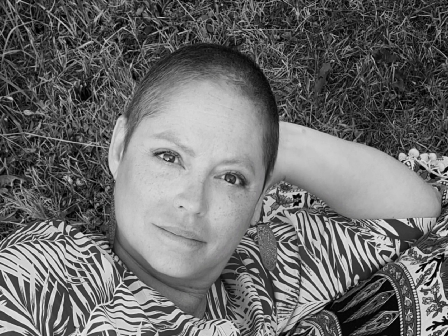 En kvinna med kort hår ligger i gräset och tittar in i kameran.