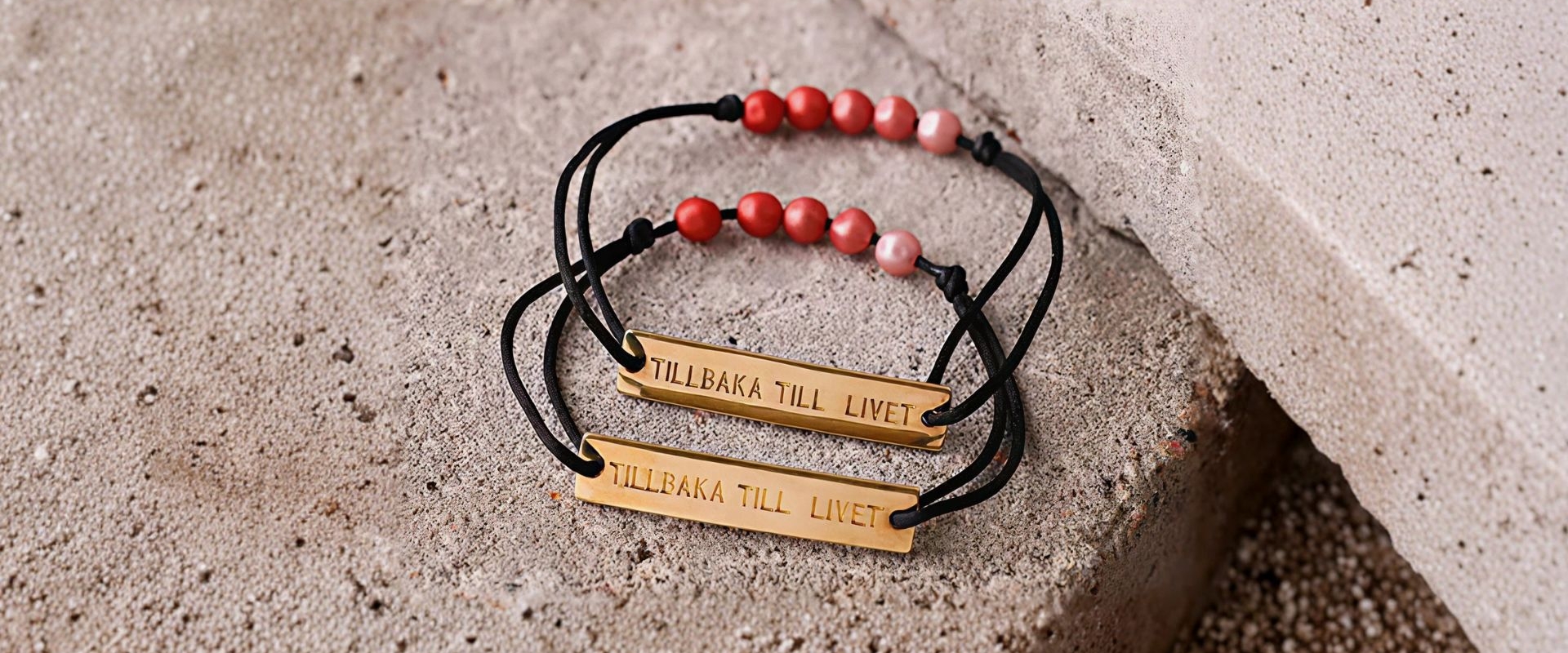 Ett armband med svart tråd, fem rosa pärlor och en bricka där det står "Tillbaka till livet".