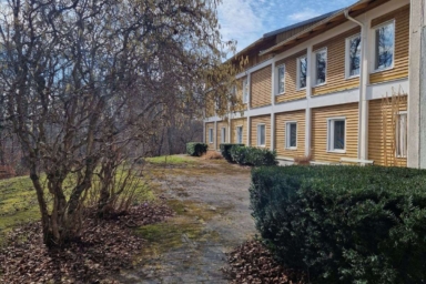 En gul träbyggnad omgiven av buskar och träd.