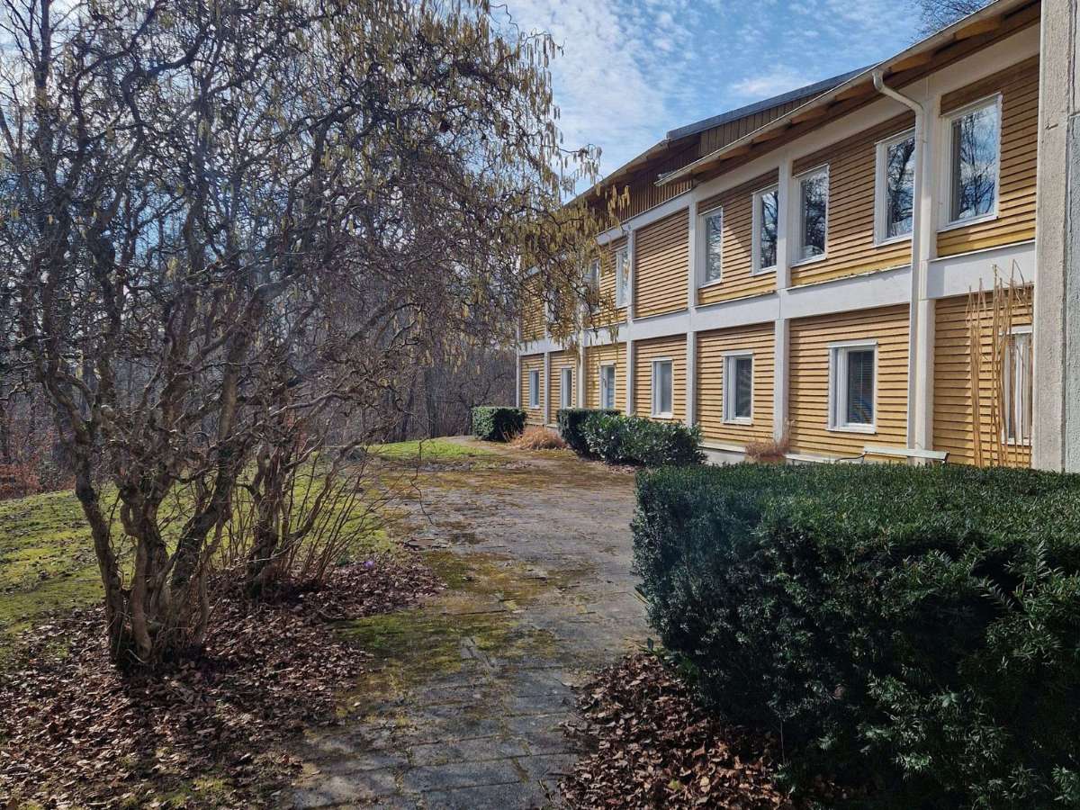 En gul träbyggnad omgiven av buskar och träd.