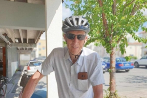 En man med cykelhjälm och solglasögon står vid sin cykel ute på gatan.