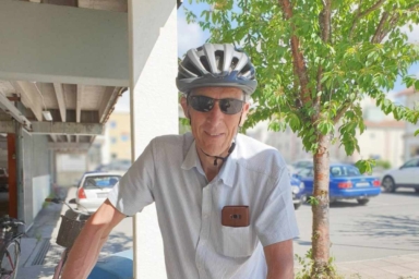 En man med cykelhjälm och solglasögon står vid sin cykel ute på gatan.