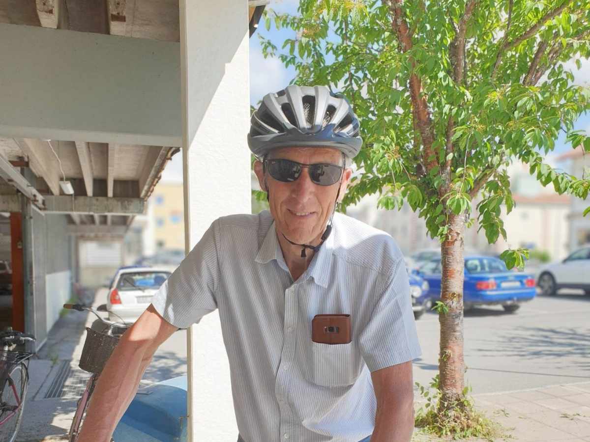 En man med cykelhjälm och solglasögon står vid sin cykel ute på gatan.